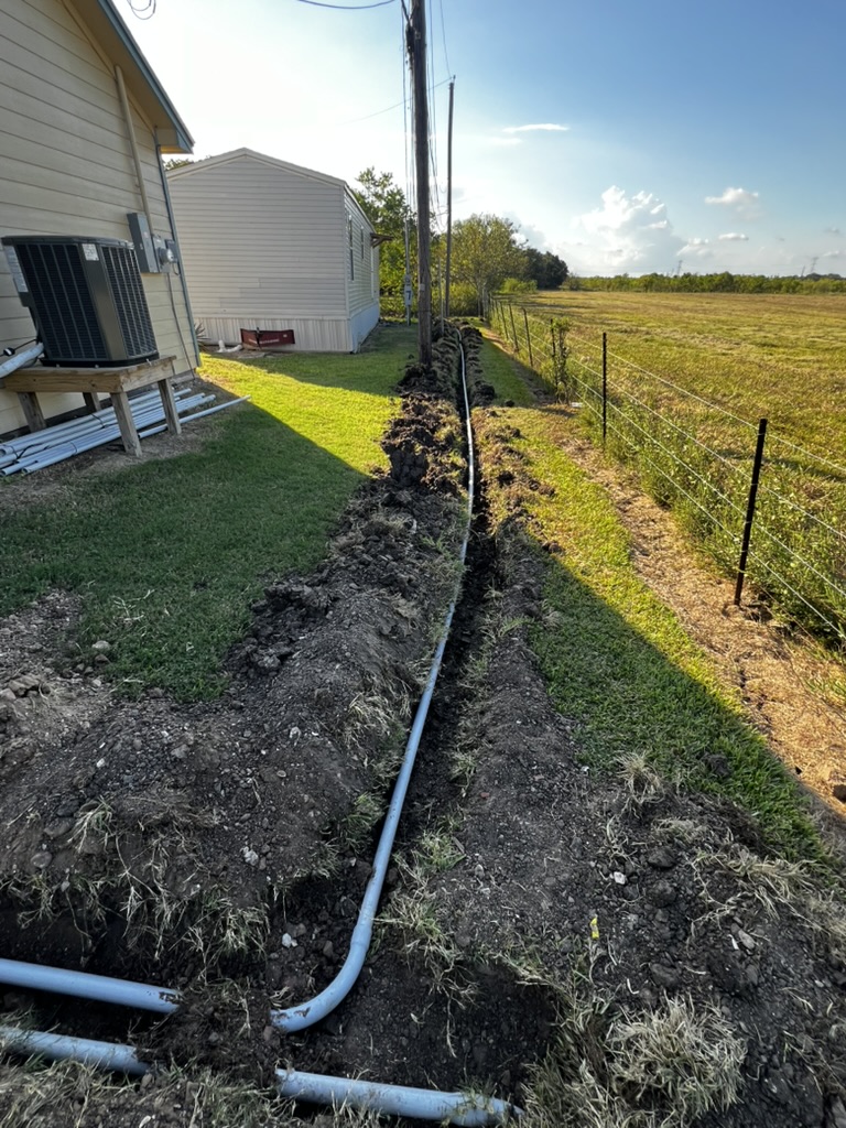 Conduit pathway laid through a long trench beside a fence and buildings.