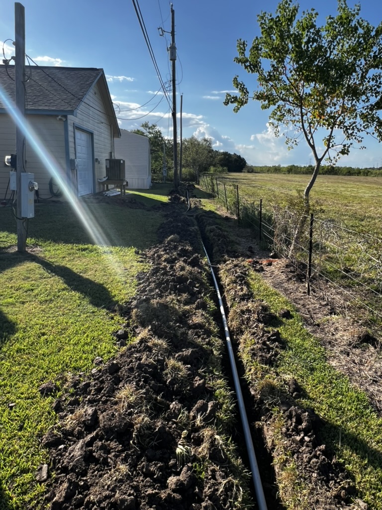 Long open trench prepared for conduit along the edge of a property.
